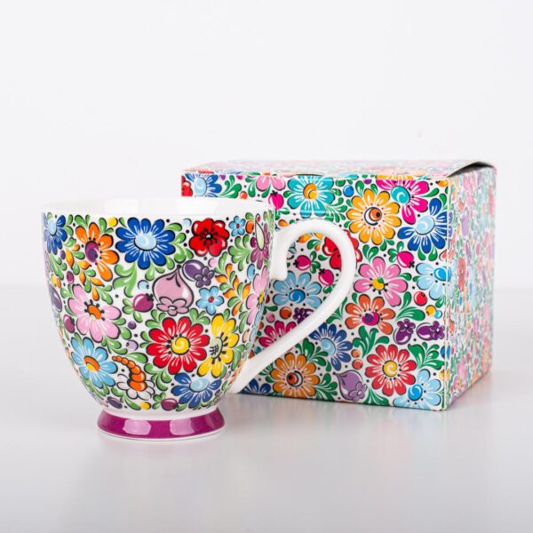 A vibrant Polish Folk Art Mug featuring hand-painted traditional Łowicz floral designs in a multitude of bright colors on a white ceramic background, shown alongside a matching decorative box with the same colorful floral pattern. The mug has a purple base.
