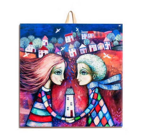 Ceramic tile with a colorful illustration of a couple holding a house together, with a whimsical town and trees in the background.