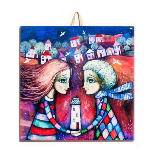 Ceramic tile with a colorful illustration of a couple holding a house together, with a whimsical town and trees in the background.